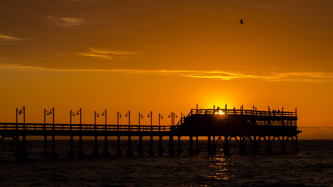 Topic is Travel Destination to Namibia. A silhouetted pier in Swakopmund, Namibia with gorgeous orange skies.