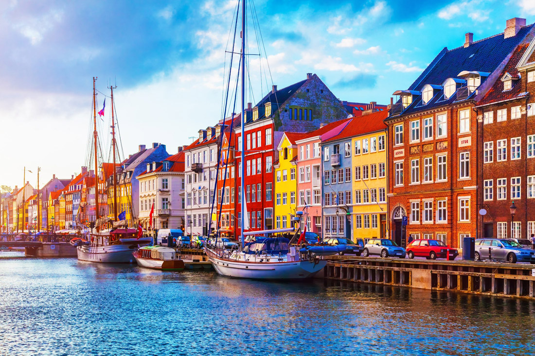 Captivating sunset hues illuminate Nyhavn pier, revealing colorful buildings, ships, and boats in Copenhagen's Old Town.