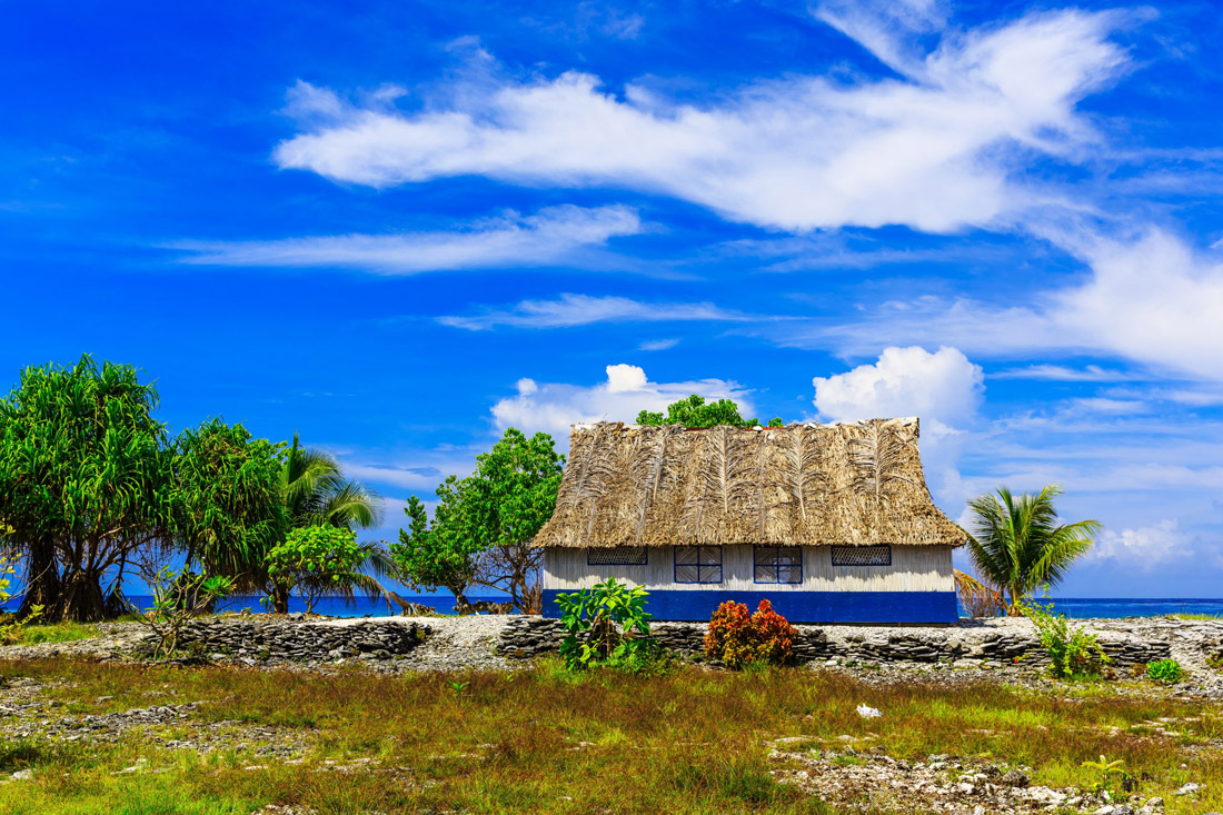 Topic is Travel Destination to Kiribati. A traditional house at Tabuaeran Fanning Island, Republic of Kiribati, overlooking sunny blue skies.