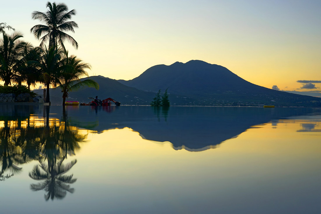 Topic is Travel Destination to Saint Kitts and Nevis. Sunset view of the Nevis Peak volcano across serene water.