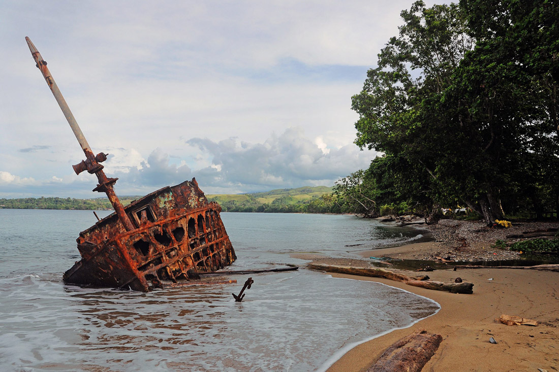 Topic is Travel Destination to Solomon Islands. Old crashed ship resting on the shore on a clear day.