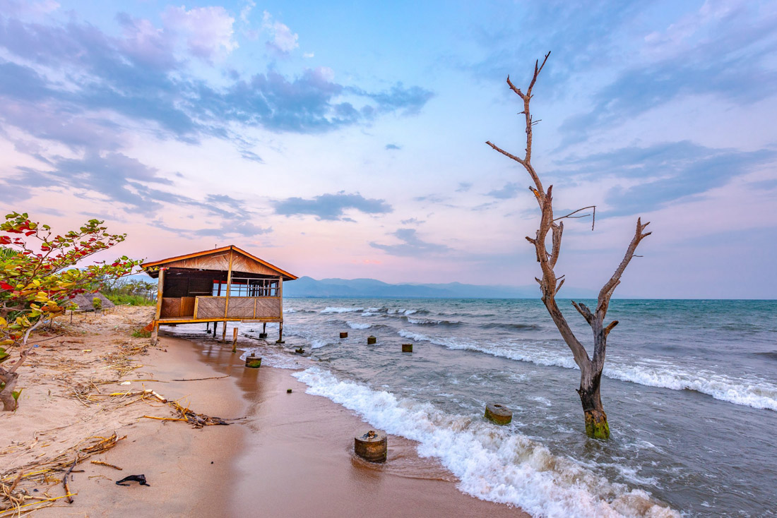 Breathtaking sunset over Lake Tanganyika in Burundi, East Africa, with a sandy beach and rustic wooden house against a windy cloudy sky.
