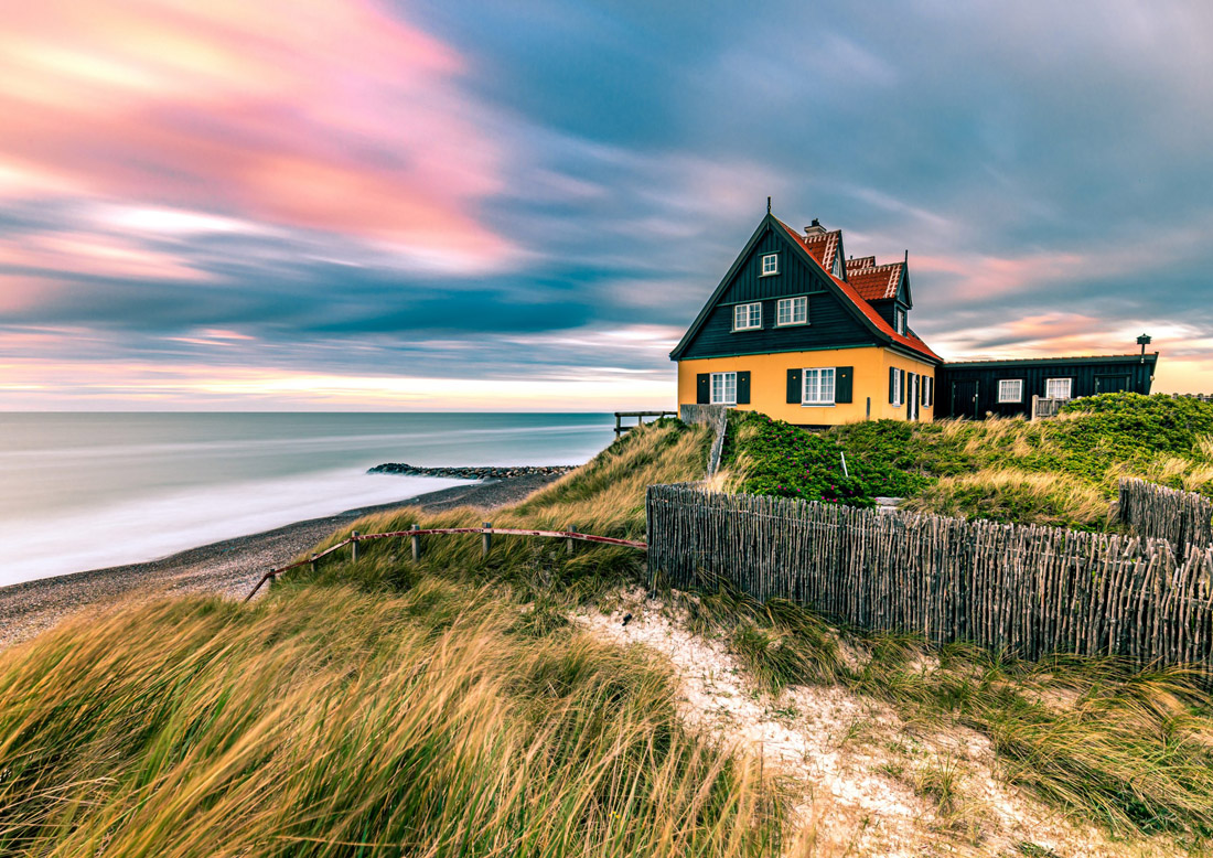 Yellow house on Skagen's beachfront with a vibrant sunset over Denmark's North Sea.