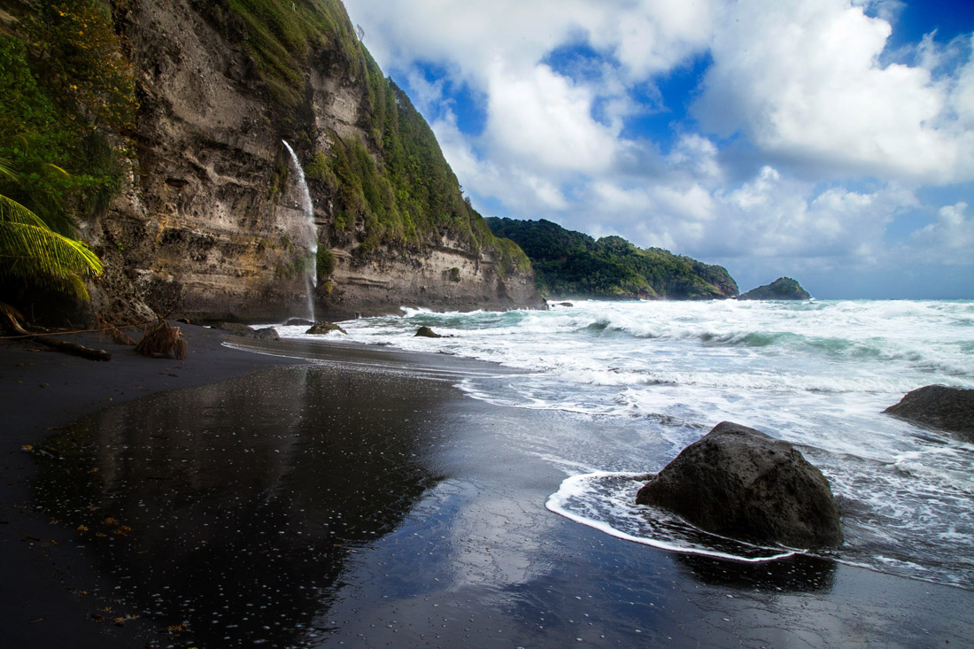 Waterfall cascading onto a black sand beach at Wavine Cyrique, Dominica.