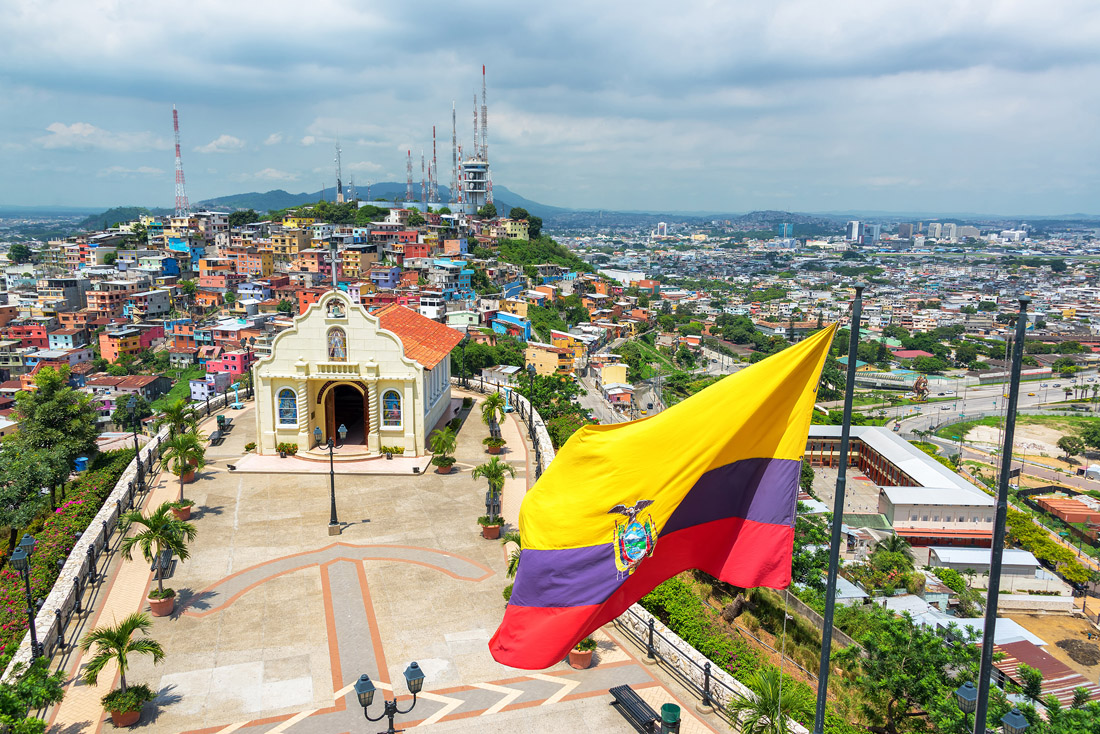Ecuadorian flag soaring above Santa Ana Hill with Guayaquil cityscape and church in backdrop.