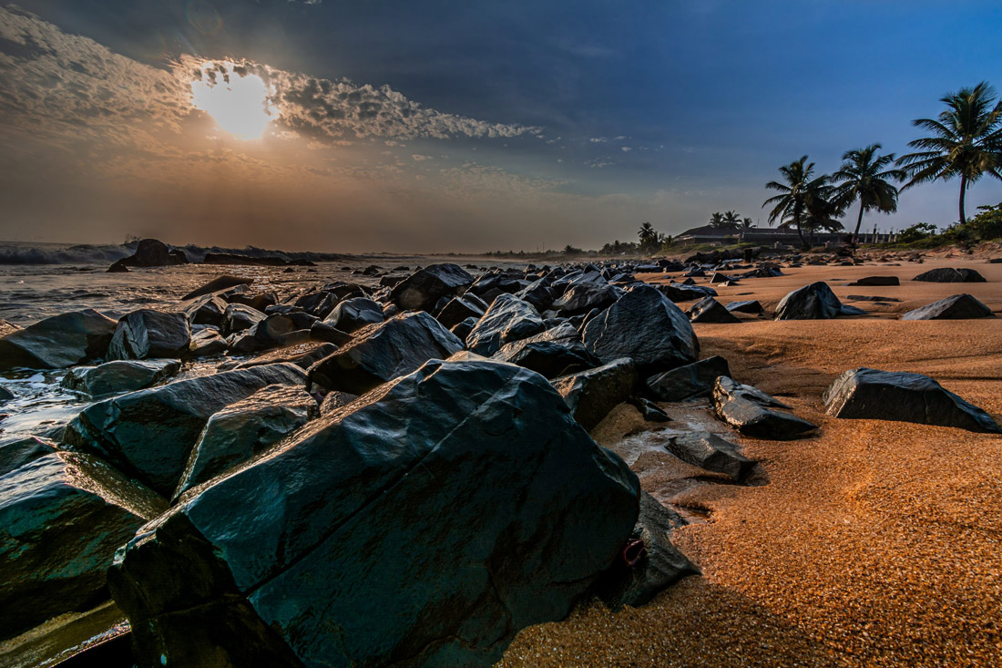 Serene beach of Congo Town, Monrovia, Liberia, with red sand, black rocks, and a stunning sunset.