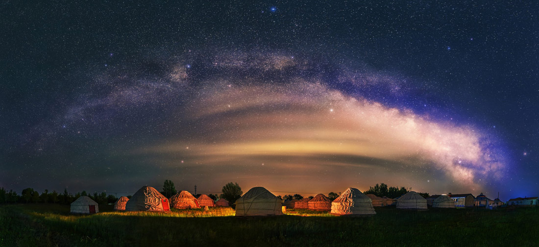 Mongolian yurts scattered on grassland under the bright Milky Way.