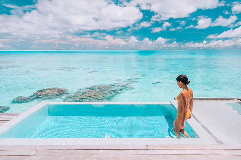 In an idyllic Bora Bora luxury resort, a woman enjoys relaxation by a private overwater bungalow pool.