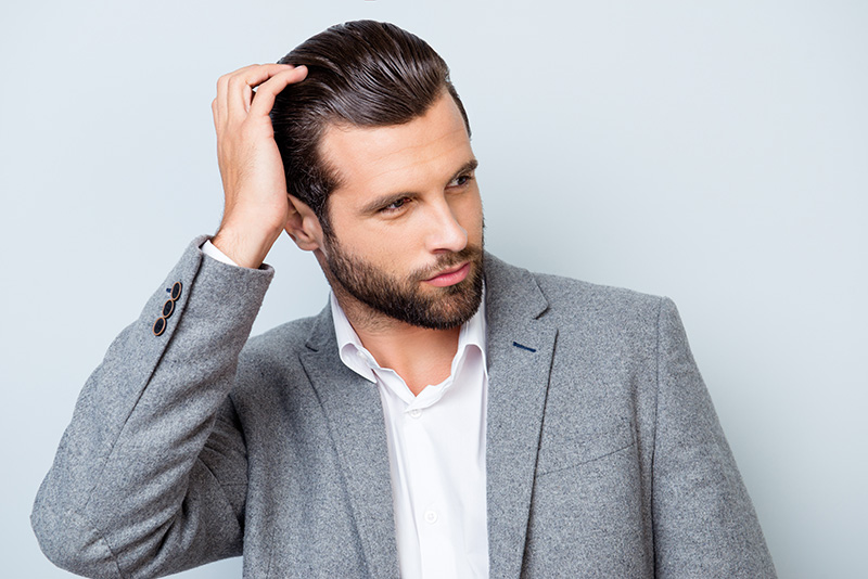 The topic on this page is hair as it pertains to beauty, maintenance, hair styles, hair cuts, hair color, etc. Close up portrait of handsome confident masculine man in jacket touching his hair.