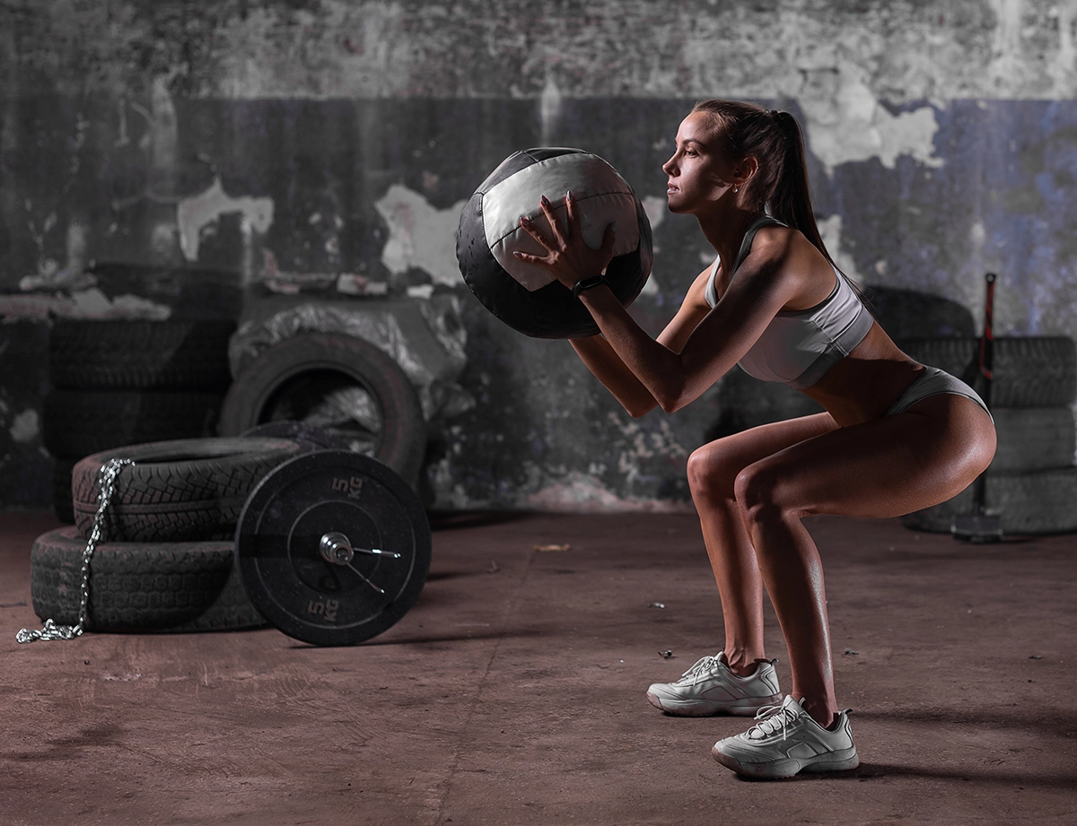 The Topic is Fitness. Muscular woman doing intense squats with medicine ball in gym.