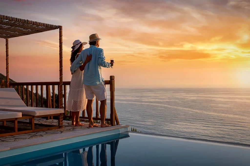 The Topic is Social Media Influencers. A romantic couple on summer vacation enjoys the sunset over the Mediterranean Sea by the pool with a glass of Aperitif.