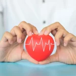 BlahFace Health Interest. Good Healthcare and Insurance Interest. Photograph of woman hand holding red heart with heart rate on blue background. Love and Family.