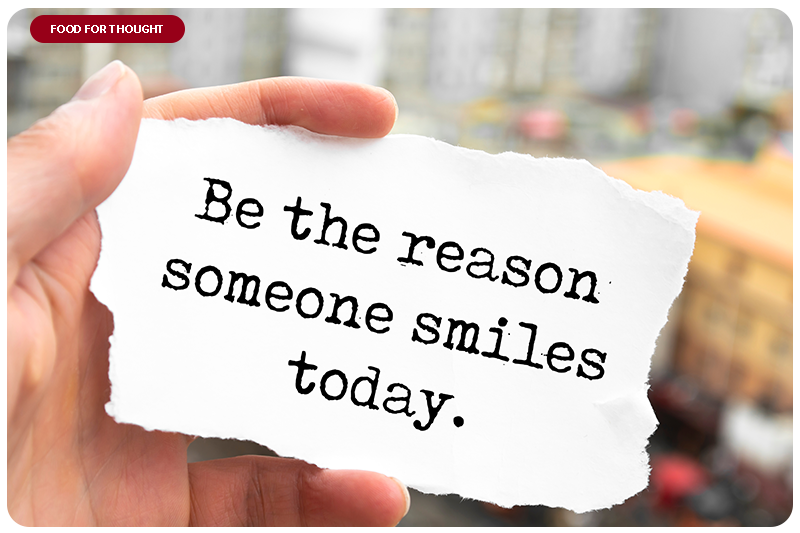 Hand holding up a motivational sign that says "Be the reason someone smiles today"